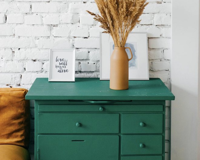 Green drawer that has a vase with flowers on top and a picture frame